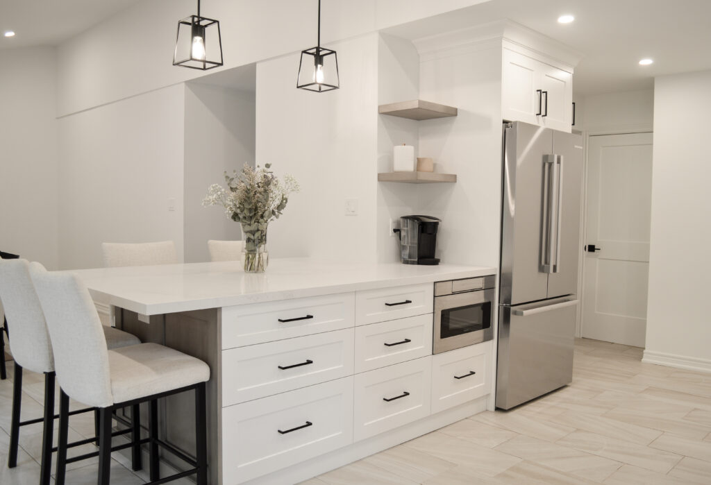 kitchen cabinets Mississauga – modern white shaker cabinets with large island, black handles, and stainless steel fridge