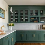 Dark green kitchen cabinets in Mississauga with glass-front upper doors, brass hardware, and a marble backsplash with L-shaped countertop.
