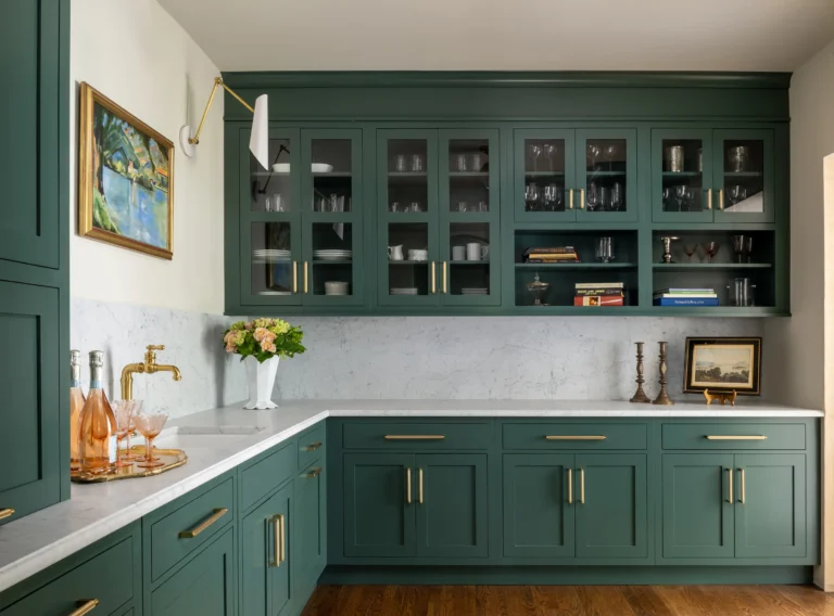 Dark green kitchen cabinets in Mississauga with glass-front upper doors, brass hardware, and a marble backsplash with L-shaped countertop.