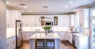 Bright modern kitchen with white shaker-style IKEA kitchen cabinets, large center island, pendant lighting, and stainless-steel appliances.