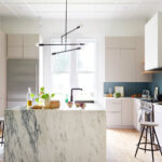 Modern minimalist kitchen featuring IKEA kitchen cabinets with flat-panel fronts, blue tile backsplash, open shelving, and a marble waterfall island.