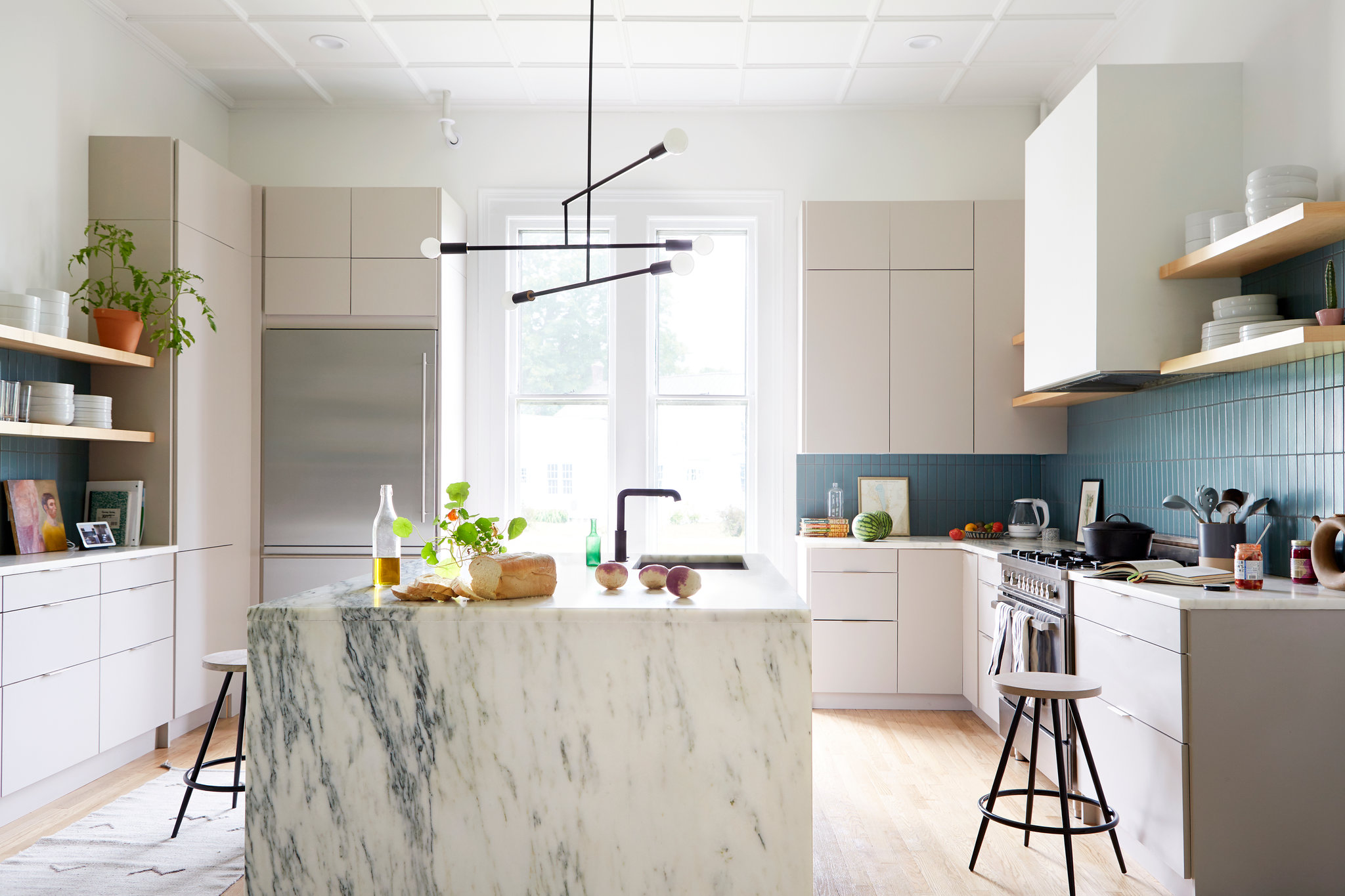 Modern minimalist kitchen featuring IKEA kitchen cabinets with flat-panel fronts, blue tile backsplash, open shelving, and a marble waterfall island.