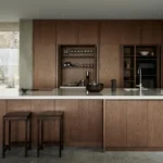 Modern minimalist kitchen with wood cabinets, white island countertop, built-in shelves and bar stools