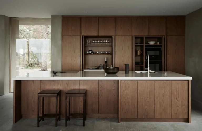 Modern minimalist kitchen with wood cabinets, white island countertop, built-in shelves and bar stools