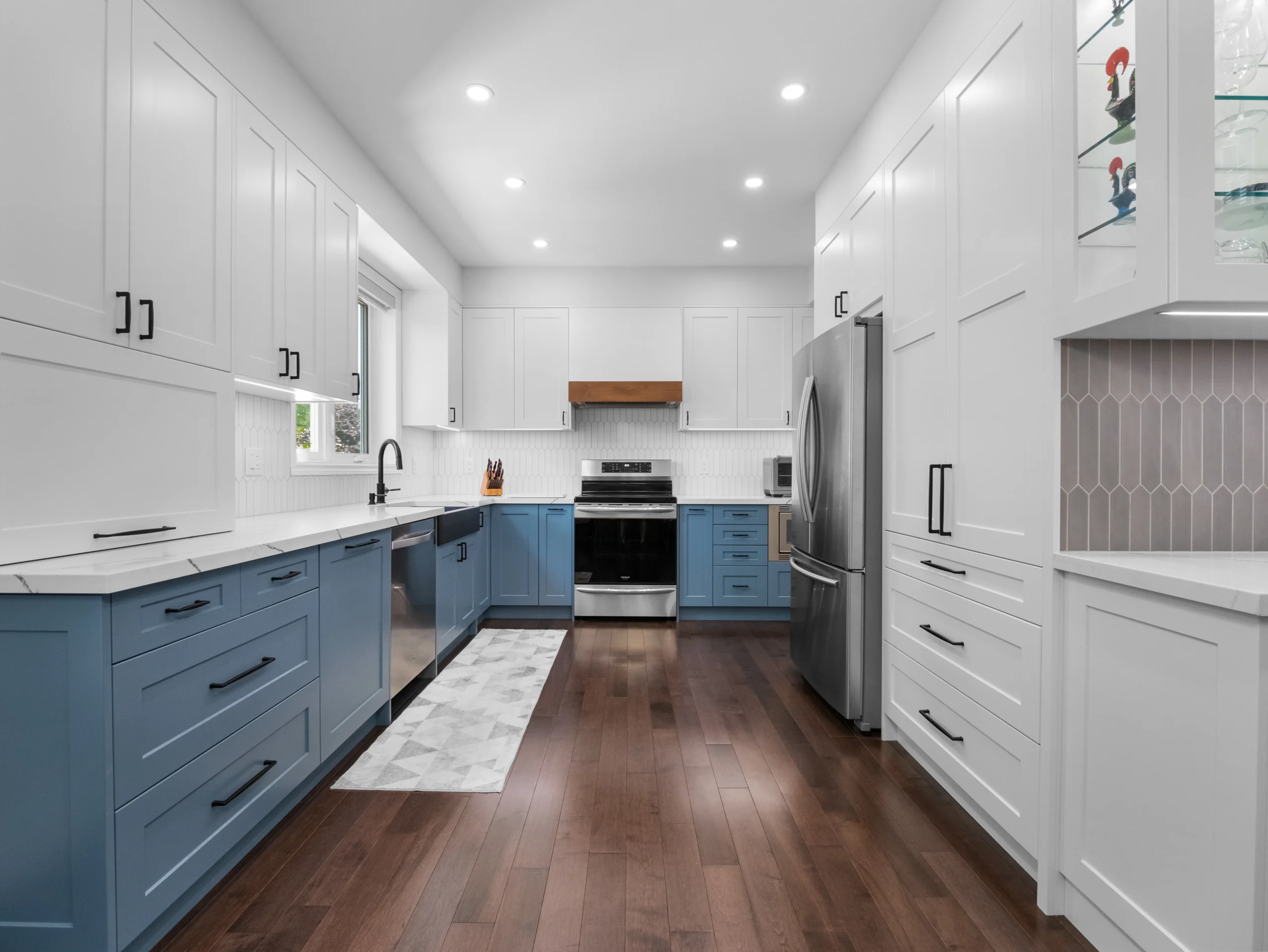 Modern two-tone kitchen cabinets Mississauga renovation featuring white shaker uppers, blue base cabinets, matte black hardware, quartz countertops, and stainless steel appliances.