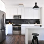 Minimalist white kitchen with flat-panel cabinets, black backsplash, stainless steel appliances, and pendant lights, illustrating a sleek contemporary layout for what are IKEA kitchen cabinets made of content.