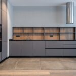 Modern minimalist kitchen featuring IKEA style kitchen cabinets in matte gray with flat-panel doors, black countertop, wood backsplash, and built-in appliances.
