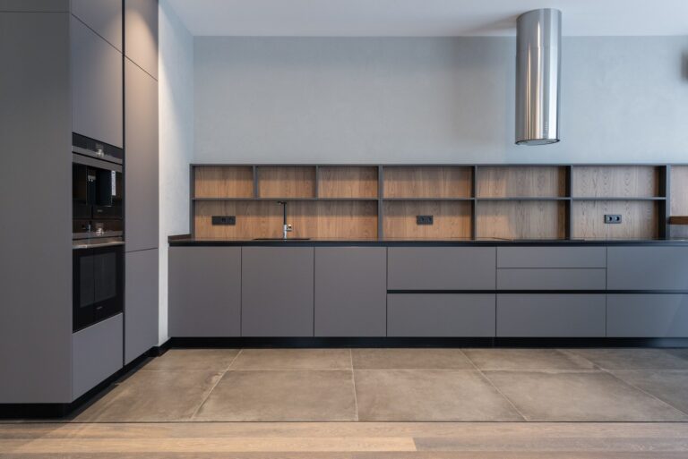 Modern minimalist kitchen featuring IKEA style kitchen cabinets in matte gray with flat-panel doors, black countertop, wood backsplash, and built-in appliances.