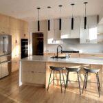 Modern kitchen featuring IKEA SEKTION cabinets with natural wood and white flat-panel fronts, a large waterfall island, black pendant lights, and minimalist open shelving.