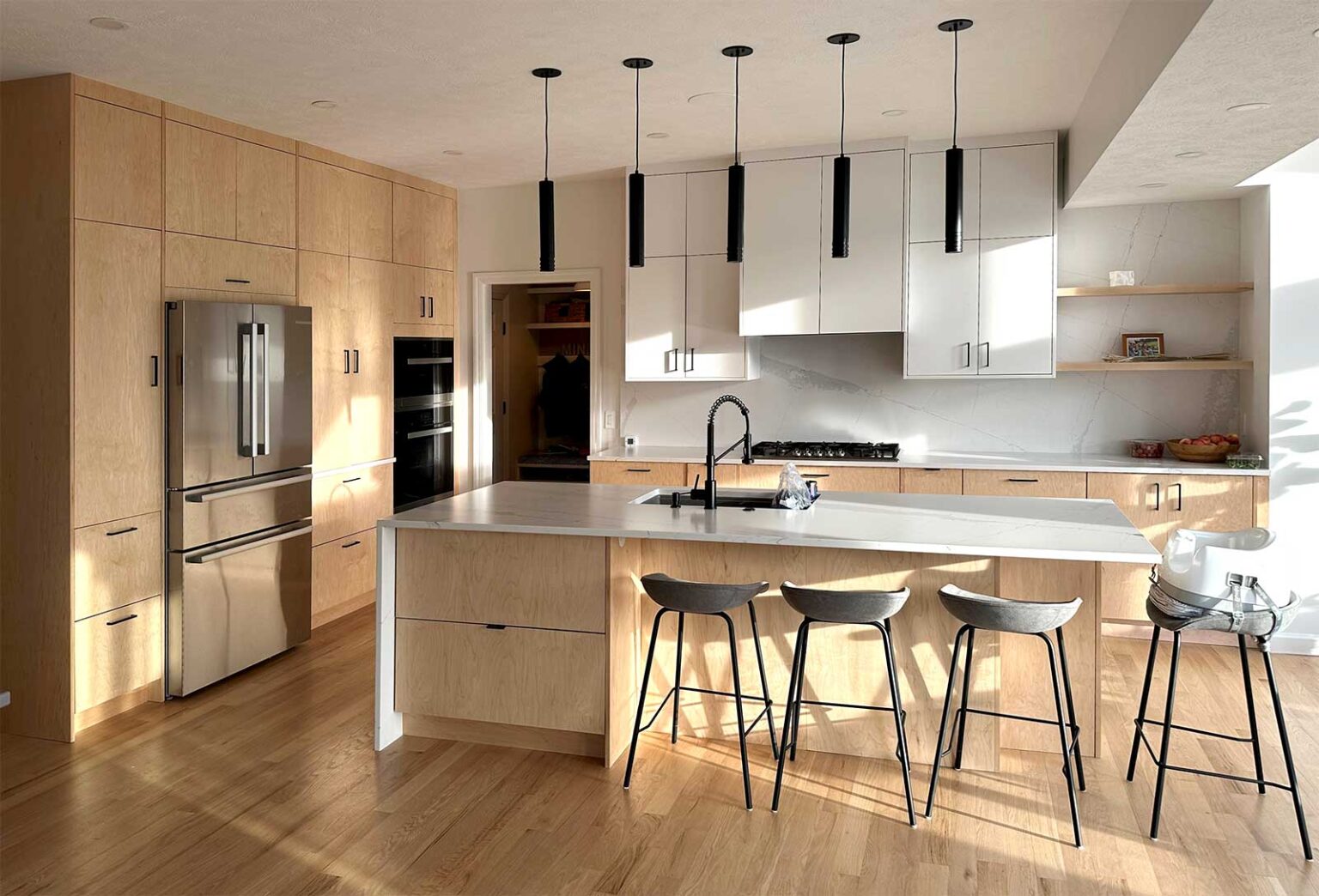 Modern kitchen featuring IKEA SEKTION cabinets with natural wood and white flat-panel fronts, a large waterfall island, black pendant lights, and minimalist open shelving.