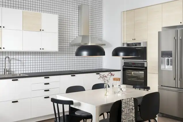 Modern IKEA kitchen with white and light wood cabinets, black accents, tiled backsplash, stainless steel appliances, and a minimalist dining table with black chairs.
